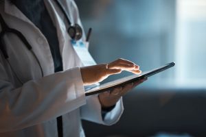 Telehealth, digital tablet and doctor hands for hospital innovation, software management and results update in dark workplace. Healthcare, cardiology and telecom medical professional with technology.